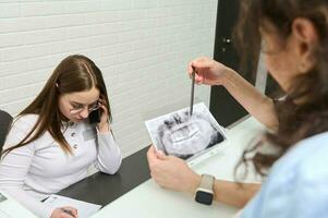 Female receptionist talks on mobile phone. Blurred foreground of a dentist holding dental x-ray panoramic radiography photo