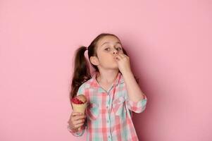 Beautiful little child girl with two stylish ponytails, holding ice cream, making delicious gesture over pink background photo