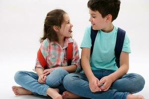 Adorable brother and sister, smart school kids with backpacks, smiling, making faces, showing tongue isolated on white photo