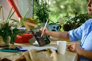 Close-up woman florist, event manager, flower designer sketching, drawing floral compositions on digital tablet photo