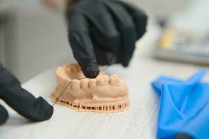 Focus on hands of dentist in black sterile gloves using dental floss showing how to brush teeth on plaster cast of teeth photo