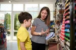 Teenage schoolboy asking help to a manager while shopping for school stationery in office supply store. Back to school photo