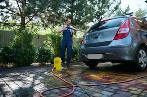 Full length portrait of young adult man washing his car under high pressure water outdoors. People Transport Technology photo