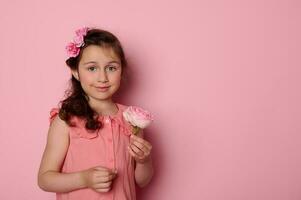 Caucasian lovely child girl in stylish pink dress, holding a beautiful rose flower, smiling on isolated pink background photo