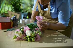 Close-up florist arranging a beautiful flower bouquet of fresh white and pink ranunculus, in floral design studio. photo