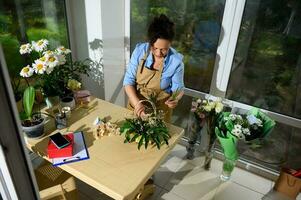 Top view florist, flower designer inserting palm leaves into soaked foam, creating floral arrangement in a wicker basker photo