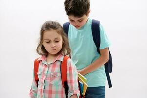 Little child girl and preteen boy prepares backpack of his sister, going to school, isolated on white studio background photo