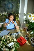 hermosa hembra florista, floral diseñador toma un café descanso durante su en línea trabajo en tableta a floral diseño estudio foto