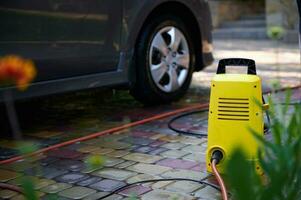Focus on a bright yellow car cleaning equipment near a car. Water high pressure cleaner, washer with hose and spray wand photo