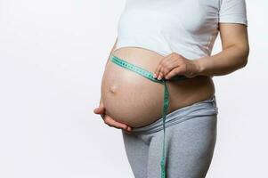 Midsection of pregnant woman measuring her belly with a tape to keep track of her fetus development, white background photo