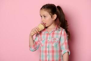 caucásico adorable pequeño niña comiendo chocolate fresa hielo crema en gofre cono, aislado terminado rosado antecedentes foto