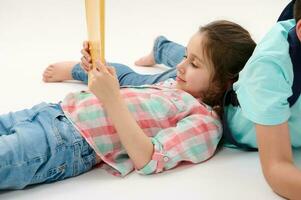 Little girl 6 y.o, first grader, primary school student in plaid shirt and blue jeans, holding textbook, white backdrop photo