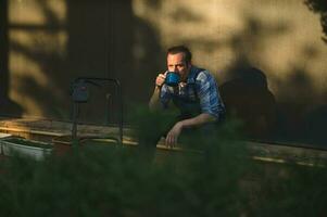 ver mediante cobertura en primer plano a profesional paisajista jardinero Bebiendo café tomando descanso después difícil trabajando día foto