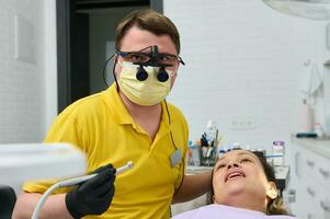 dentista en ortodoncista prismáticos, sostiene dental perforar, realiza dientes tratamiento a embarazada paciente en odontología clínica foto