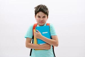 Irritated angry schoolboy holding workbooks, expresses negative emotions, feels unhappy to start new semester at school photo