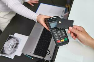 parte superior ver cliente mano sostiene negro Bosquejo crédito tarjeta encima un pos Terminal, hace sin efectivo pago utilizando nfc tecnología foto