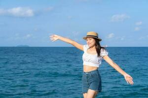 mujer joven feliz levantando las manos y parada en el puente con fondos oceánicos tropicales, disfrutando de la hermosa vista del mar azul. estilo de vida de verano al aire libre. concepto de vacaciones y libertad. foto