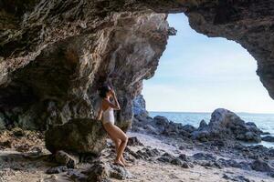 Portrait of beautiful fashionable woman in white bikini posing at the rock beach. Young Asian woman dressed in swimsuit standing on a rock on summer day with sunset backgrounds at Koh Larn in Pattaya photo