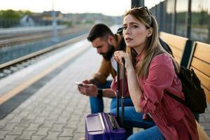 Anxious and tired couple sitting at railway station and waiting for arrival of their train. photo