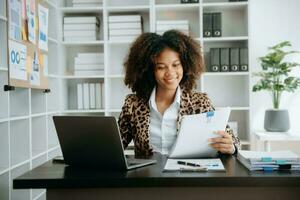 Young beautiful African woman typing on tablet and laptop while sitting at the working wooden table modern office photo