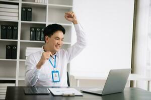 Young Asian business man using laptop and tablet while sitting at her working place. Concentrated at work. photo