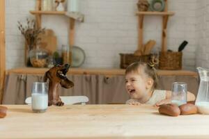 un pequeño contento niña jugando con un perro tejonero perro en el cocina foto