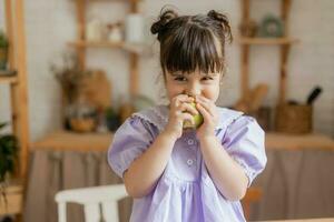 un pequeño hermosa niña en un brillante vestir es engañando alrededor en el cocina foto