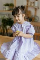 un pequeño hermosa niña en un brillante vestir es engañando alrededor en el cocina foto