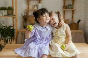 pequeño contento muchachas tonto alrededor en el cocina y comer manzanas foto
