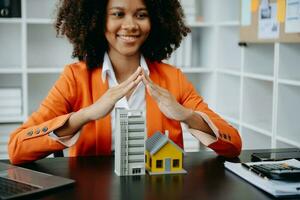 African Female real estate agent is use hands to protect red roof for the concept of real estate investment about house trading, purchase at desk photo