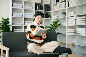 Young Asian woman listening music from headphones and writing note for her work idea in diary book.She in home office or cafe photo