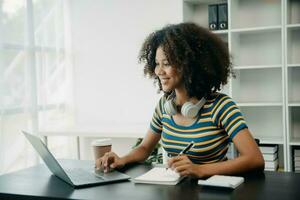 Young attractive Africanfemale office worker business suits smiling at camera with working notepad, tablet and laptop documents photo