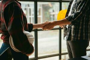 Engineers or architecture shaking hands at construction site for architectural project, holding safety helmet on their hands. photo