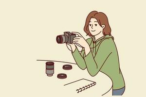 mujer fotógrafo con cámara se sienta a mesa elegir lente para foto ensayo o creando retrato de interlocutor. niña con cámara trabajos como periódico fotógrafo tomando imágenes para Noticias publicaciones. vector