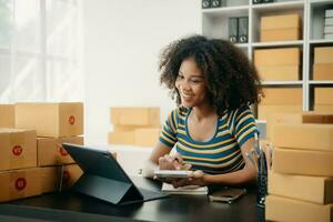 puesta en marcha pequeño negocio pequeño, empresario propietario africano mujer utilizando teléfono inteligente o tableta tomando recibir y comprobación en línea compra compras orden foto