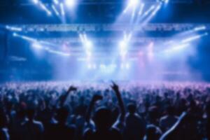 blurred crowd audience watching and listening live show on stage in concert hall. group of people together in stadium with fantastic lighting effect background. photo