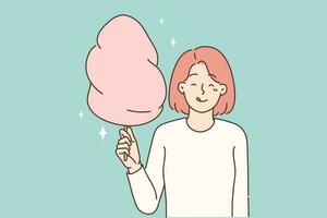 Cheerful girl with cotton candy in hands licks lips in anticipation taste of street dessert bought during walk in park. Positive woman holding appetizing sweet cotton candy for happy childhood concept vector