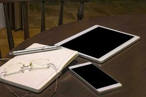 Office table, mobile phone, tablet, glasses, notebook and pen with copy space. Gadgets on a wooden table. photo