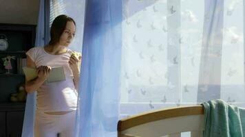 Future young mother between 30 and 35 years old is reading a book close to the open window. video