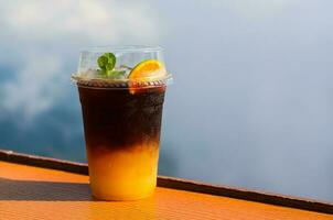 A glass of iced coffee mixes with orange juice put on table with sky and cloud background. Summer drink concept. photo