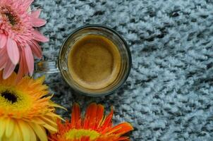 A glass of Espresso coffee shot puts on bed with Gerbera flowers. Stay home concept. photo