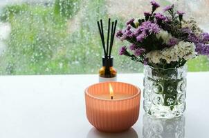 Flame burning at aroma candle puts near by window with rain drop in monsoon season. Zen and relax concept. photo