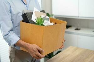 Business man sending resignation letter and packing Stuff Resign Depress or carrying business cardboard box by desk in office. Change of job or fired from company photo