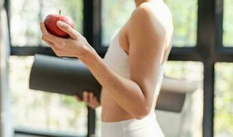 aptitud mujer participación yoga estera con Fresco manzana heathy limpiar vegano comida antes de trabajando fuera en yoga estudio foto