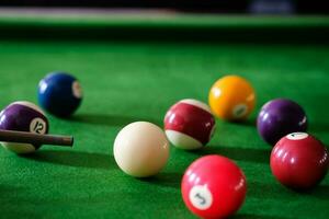 Man's hand and Cue arm playing snooker game or preparing aiming to shoot pool balls on a green billiard table. Colorful snooker balls on green frieze. photo