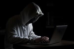 Mysterious hacker wearing a hoodie is typing on a laptop, photo