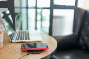 Charging mobile phone battery with wireless device in the table. Smartphone charging on a charging pad. Mobile phone near wireless charger. photo
