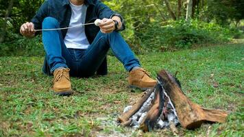 Man warm near campfire in forest and marshmallow on skewers. photo