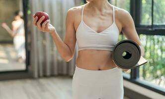 Fitness woman holding yoga mat with Fresh Apple Heathy clean vegan food before working out in yoga studio photo