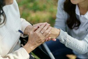 Family relationship Asian senior woman in wheelchair with happy daughter holding caregiver for a hand while spending time together photo